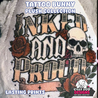 A close-up of a plush fabric product printed with a tattoo-style design reading 'Inked and Proud,' featuring a white skull, red roses, green leaves, and black linework. Large overlaid text says 'TATTOO BUNNY PLUSH COLLECTION' and 'LASTING PRINTS,' with a 'SILLY DOG DESIGNS' logo in the lower right.