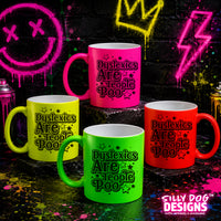 Four ceramic mugs in pink, yellow, green, and red, each printed with the phrase 'Dyslexics Are Weird Poo' in black. The mugs are arranged on dark steps against a graffiti-style background with neon paint splatters and spray cans.