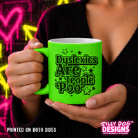 A person holds a bright neon green ceramic mug with the text 'Dyslexics Are People Poo' in black and white. The person is wearing a black knit sweater, and the background features a colorful graffiti wall with pink and yellow heart designs.