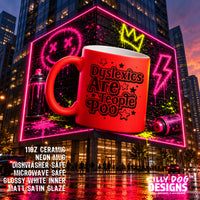 A large red ceramic mug with black and pink graffiti-style text reading 'Dyslexics Are People Poop' is shown floating in front of a neon-lit city building at dusk. The mug has glossy white interior visible at the rim and handle.