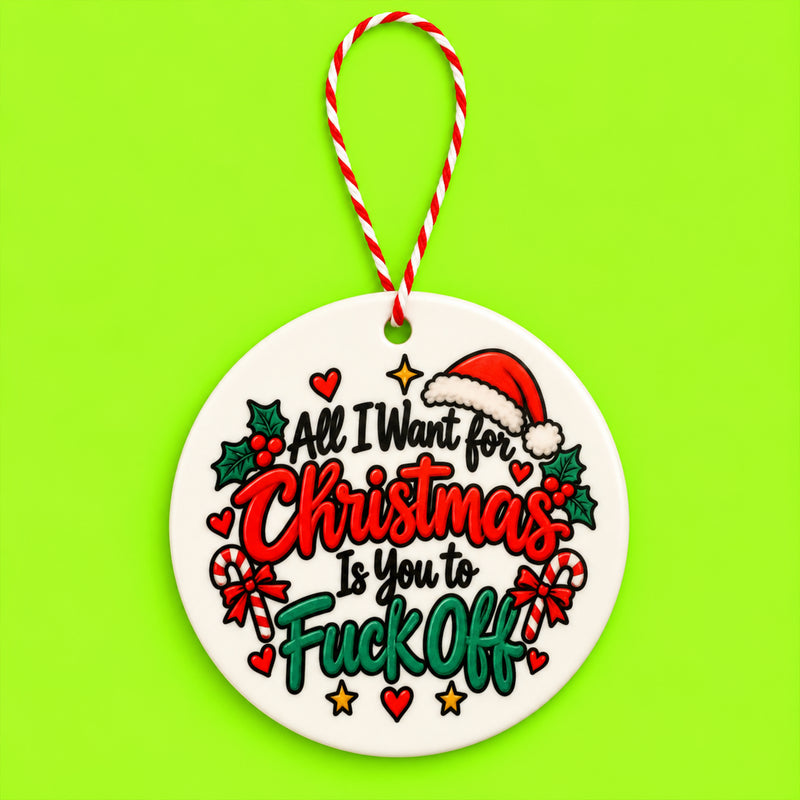 A round white ceramic Christmas ornament with a red and white striped hanging string, featuring a festive graphic with the text 'All I Want for Christmas Is You to Fuck Off' in red and green lettering, surrounded by candy canes, holly, hearts, and a Santa hat on a bright lime green background.