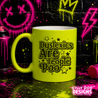 A bright neon yellow-green ceramic mug with black text reading 'Dyslexics Are People Poo' surrounded by stars, set against a graffiti-splattered black wall with spray paint cans.